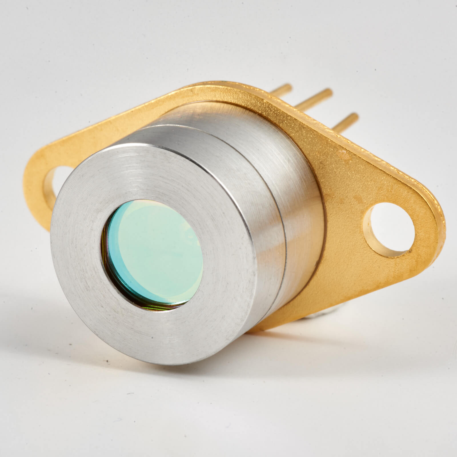 Close-up of a metallic sensor or electronic component with a circular glass window, mounted on a gold-colored base with two screw holes and four metal pins extending from the back.