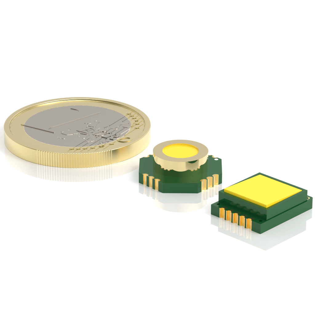 Close-up of a coin next to two small electronic components with green bases and yellow tops. The components are slightly smaller than the coin, showcasing their size for scale. The image has a reflective white surface.