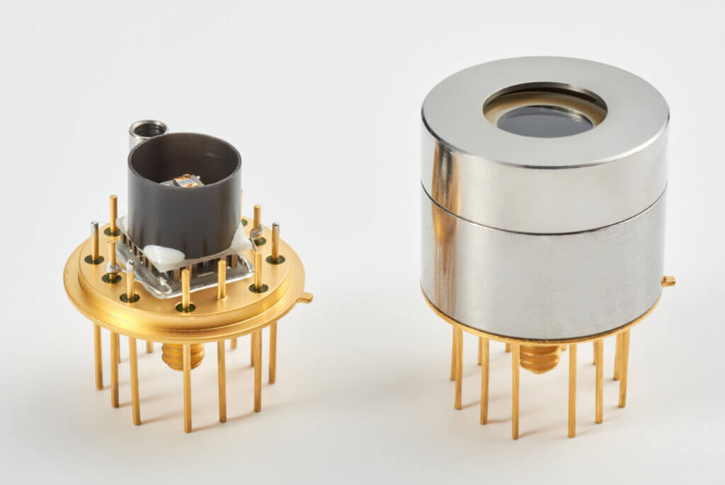 Two electronic components with gold pins, one partially exposed showing internal parts and the other covered by a shiny metallic casing, both designed for integration into electronic devices.