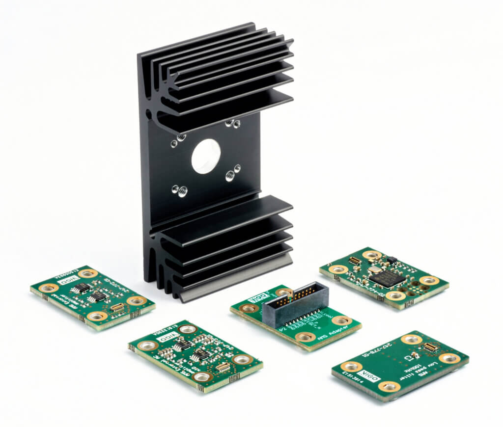Five small green circuit boards are arranged around a black metal heat sink with fins, all placed on a white background. The circuit boards have various electronic components and connectors.