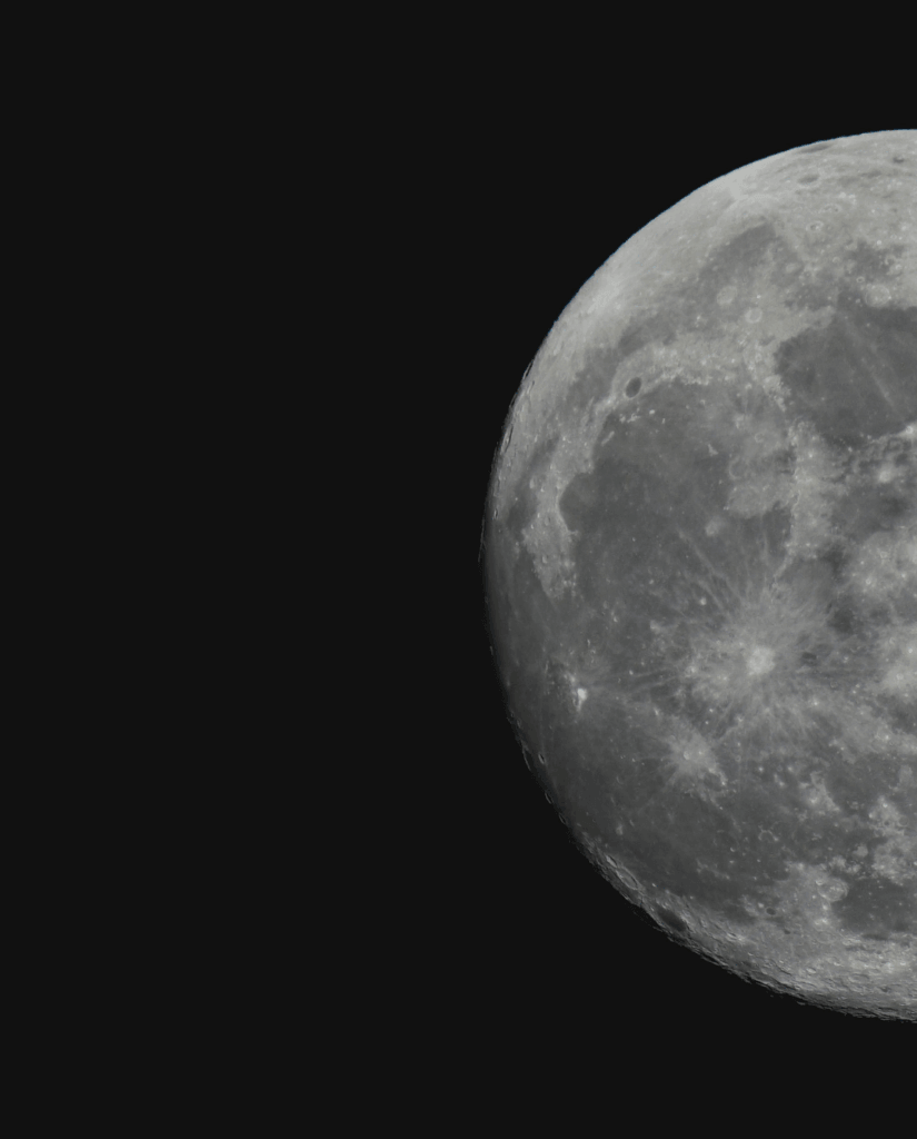 A close-up photo of the Moon against a black background, showing detailed craters and surface textures. Only part of the Moon is visible, positioned in the upper right corner of the image.