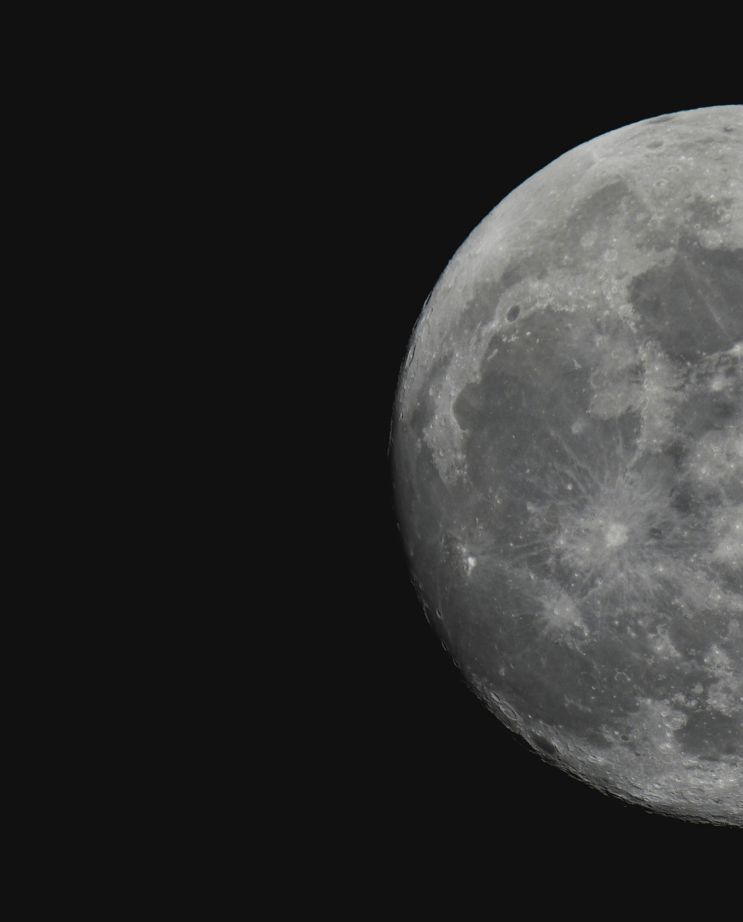 A close-up photo of the Moon against a black background, showing detailed craters and surface textures. Only part of the Moon is visible, positioned in the upper right corner of the image.