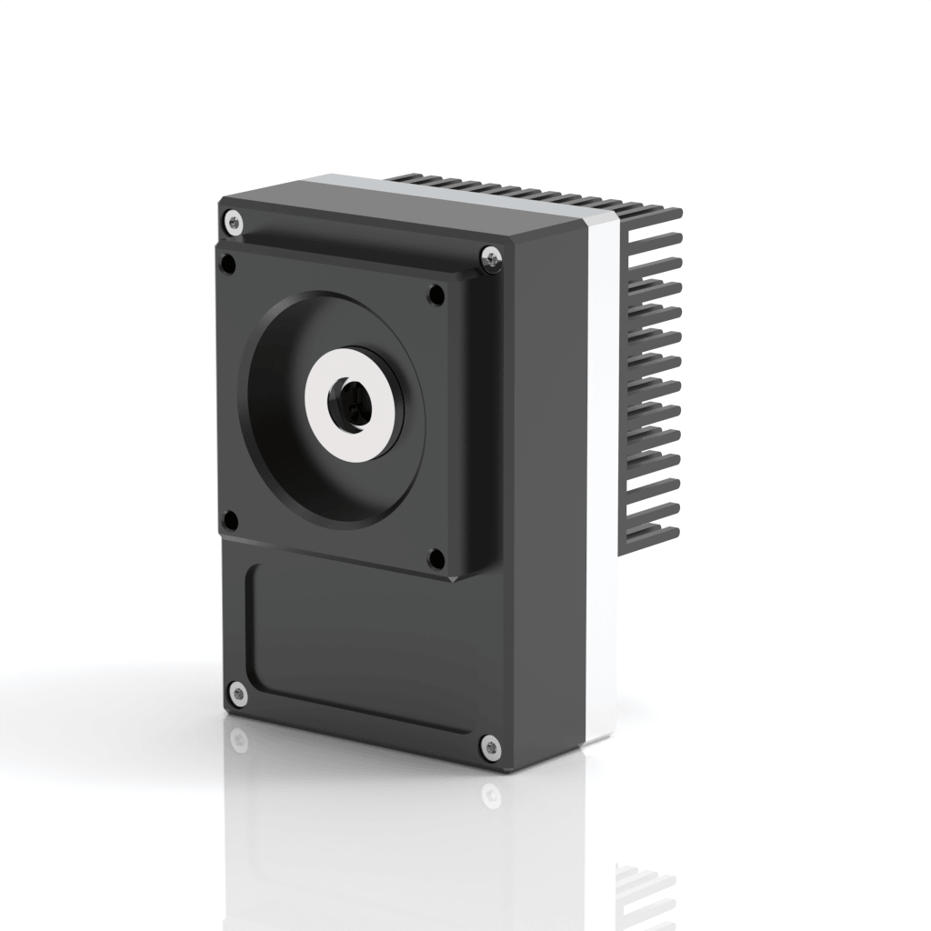 A black rectangular industrial electronic device with a central circular opening, metal fins for heat dissipation on the side, and silver screws at the corners, placed on a reflective white surface.