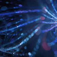 Abstract image featuring swirling blue and purple light trails against a dark backdrop. The design resembles ethereal streams or beams crossing and intertwining with glowing bokeh effects.