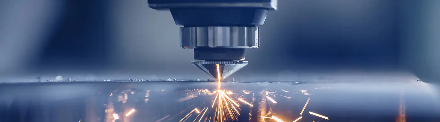 A close-up of a laser cutting machine in action, emitting bright sparks as it precisely cuts through metal. The background is blurred, highlighting the focused and intense process of laser cutting.