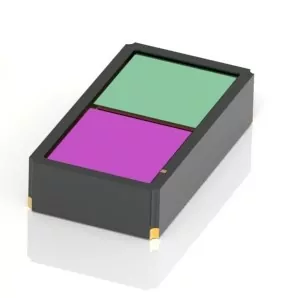 A small black rectangular device with two colored panels on top, one green and one purple, placed side by side. The device has gold contacts on its corners.