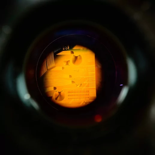 A close-up view of a circular circuit board illuminated with orange light, surrounded by darkness. The intricate components and pathways are visible, highlighting the detailed design within the glowing circle.
