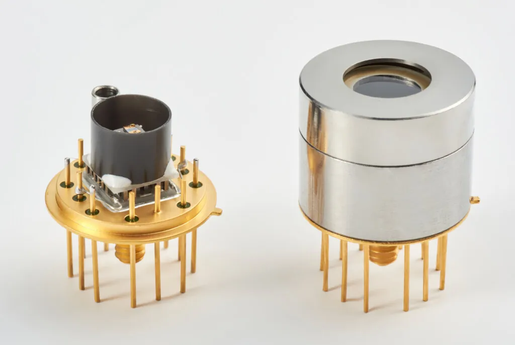 Two electronic components with gold pins, one partially exposed showing internal parts and the other covered by a shiny metallic casing, both designed for integration into electronic devices.