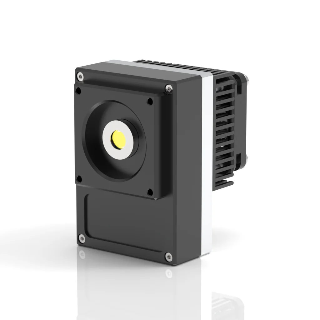 A compact, rectangular industrial device with a circular lens or sensor in the center and a finned heat sink on the back, standing on a reflective surface against a white background.