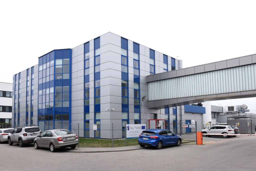 A modern, multi-story office building with blue-tinted windows and a skywalk connecting to another structure. Several parked cars are in the foreground, and the area appears clean and organized.